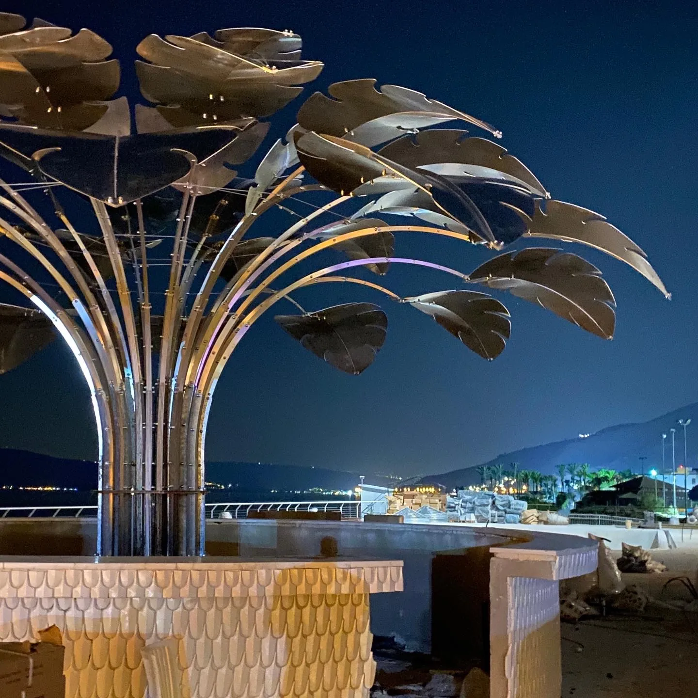 Under the edge of the canopy at night — stems and leaves against the promenade lights.