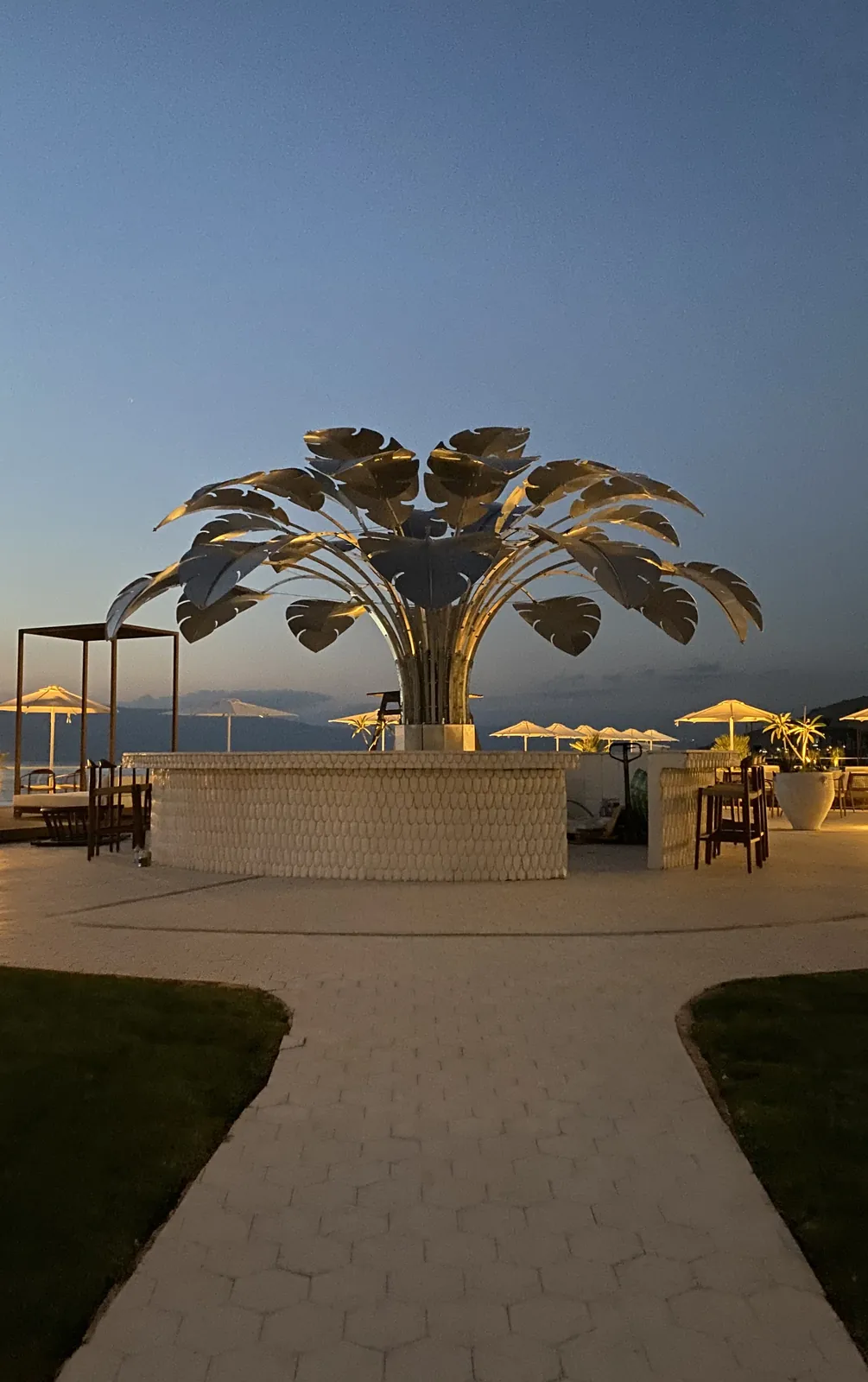Dusk from the garden path — the lit crown over the white-scaled bar.