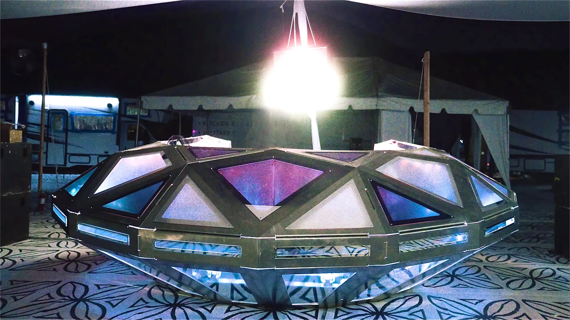 Diamond UFO مضاءة في المهرجان — خمسة وخمسون وجهًا حليبيًّا يتوهّج حول المنصة. لقطة من فيديو، لا صورة فوتوغرافية.