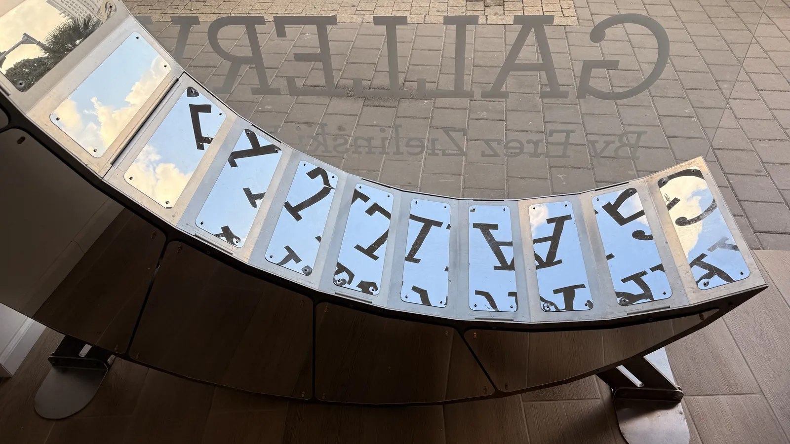 Close view of Moon Chair seat plates in mirror and brushed stainless, reflecting window lettering.