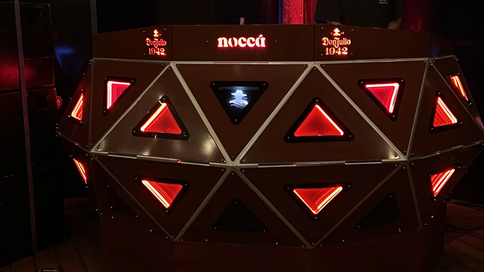 Tight frontal crop of the lit console filling the frame: red triangular panels alternating point-up and point-down across two bands, one blue-white panel carrying the Don Julio figure, and the glowing top rail with 