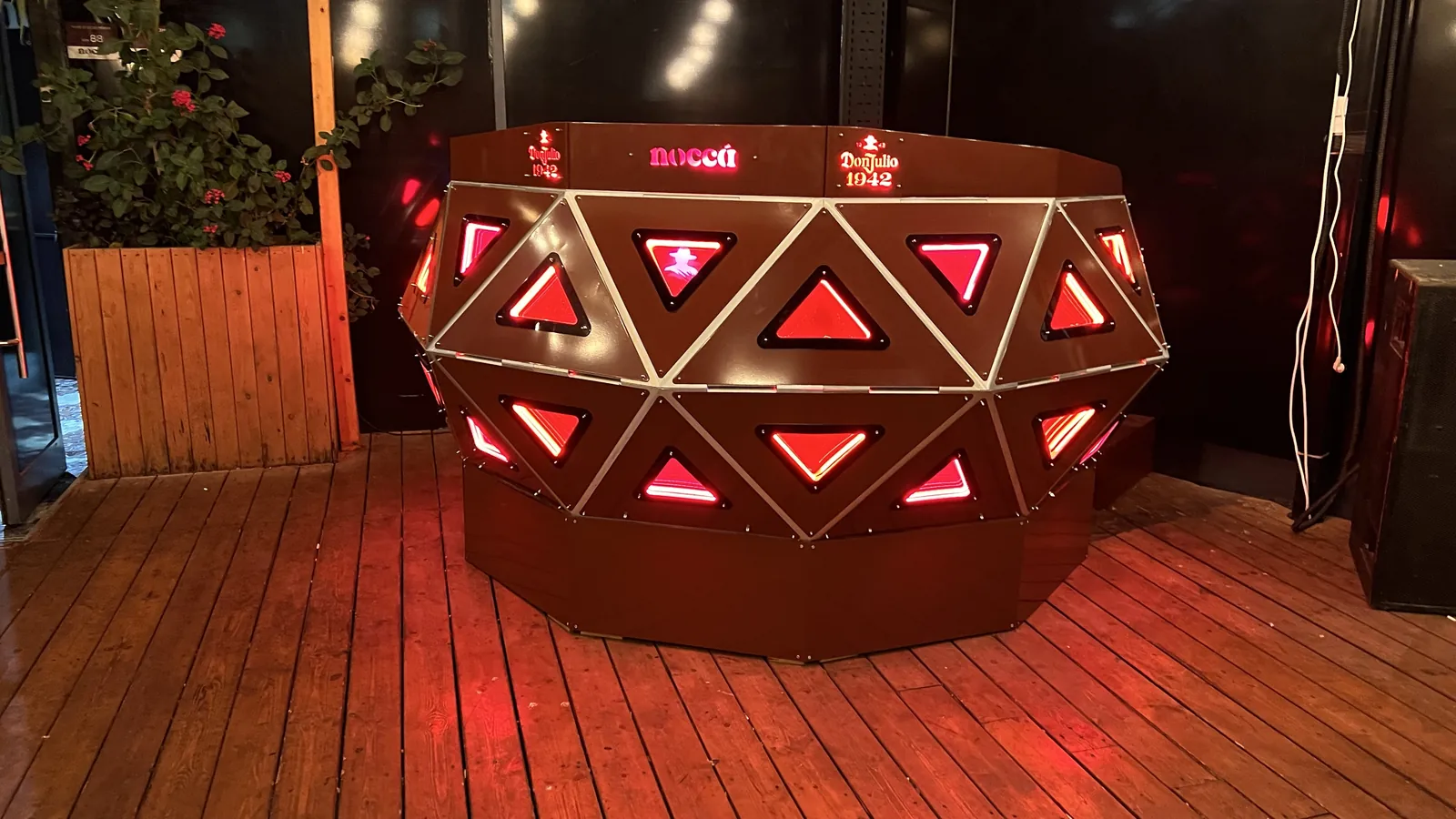 The whole curved body seen from the front with both wings sweeping back, upper and lower bands of red triangles lit, the top rail carrying Don Julio 1942 twice around noccá, on bare deck boards.