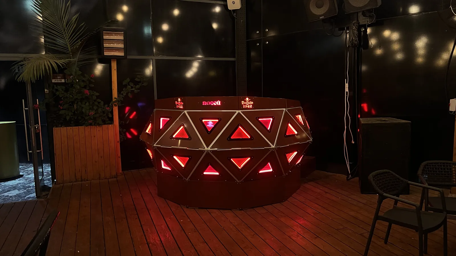 The same terrace framing a stop darker, the console reduced to two bands of red triangles and three lit words floating in near-black, the deck barely catching the glow.