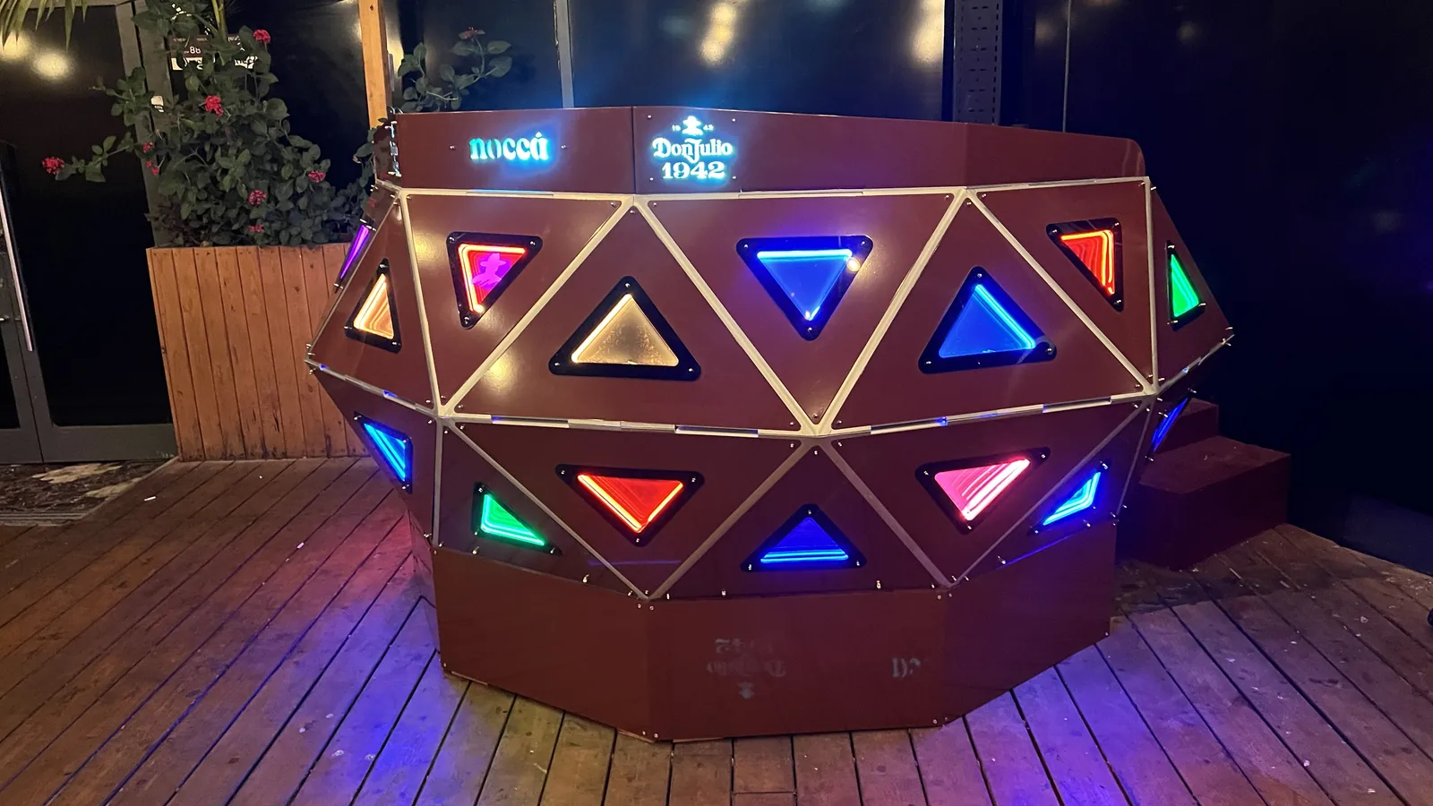 The console at night with its panels running mixed colour instead of red, blue, green, amber, magenta and red triangles scattered across both courses, the lettering lit cool white, and the deck around it washed violet.